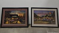 Photo of two framed Dave Barnhouse prints side by side showing detailed evening street and gas station scenes.