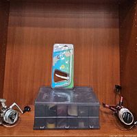 Fishing bundle arranged on shelf including three fishing reels to sides, a plastic tackle box in center, and a new Ban Hookout fishing tool on top of the tackle box.