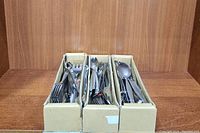 Three cardboard boxes filled with assorted stainless steel forks and spoons, showing overall lot contents