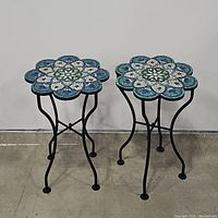 Pair of floral mosaic metal plant stands showing floral patterned mosaic tops and curved metal legs.