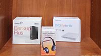 All three boxed items together: Memorex DVD Writer 8x, Seagate Backup Plus 3TB, and noise-cancelling headphones in their packaging