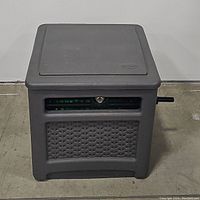 Closed view of grey Suncast hose reel storage box with basket weave design and lid closed, showing compact square shape and side crank handle.