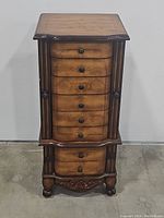 Closed front view of the wooden 8-drawer jewelry armoire cabinet showing curved drawers and carved base.