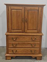 Front view of the oak armoire showing two-door cabinet on top and four drawers below with metal handles.
