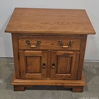 Front view of oak nightstand showing drawer and two doors closed with brass handles and wooden accents