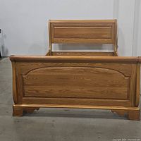 Front view showing the curved sleigh bed footboard with raised paneled design and arch detail.