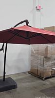 Side view of open red patio umbrella showing canopy and supporting frame against warehouse background.