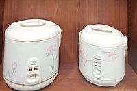 Both rice cookers side by side on a wooden shelf showing their overall shape and floral pattern.