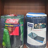 Front view of Coleman Base Camp and Wenzel Timberwolf king size sleeping bags in their storage bags.