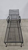 Full view of wrought iron chaise lounge showing length and mesh design seat and backrest.