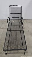 Full view of the wrought iron chaise lounge showing mesh seating and backrest, armrests, and wheels.