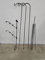 Full lot showing three shepherd's hooks, decorative bird stake, and five garden stakes leaned against a wall.