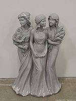 Front view of a solid garden statue featuring three women standing together in flowing dresses, holding flowers and plants.