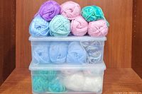 Stacked plastic containers filled with yarn skeins in pastel shades.