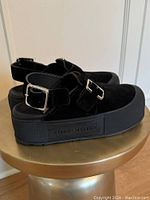 Side profile of both clogs on a pedestal showing suede uppers, platform sole and embossed logo