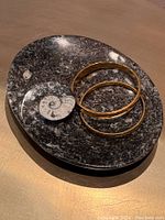 Top view of the oval stone dish showing the ammonite fossil detail with two gold bracelets placed on the dish.