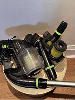 Bissell cordless vacuum main unit, attachments including brush and extension tubes, extra filter lying on round table.