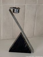 Photo of candle holder showing black marble pyramid base and angled chrome candle cup, front angle.