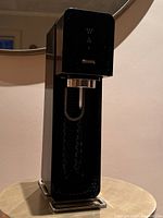 Glossy black SodaStream carbonation machine on table with sleek modern design.