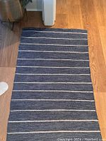 Full view of rectangular muted royal blue runner rug with narrow white horizontal stripes on hardwood floor.