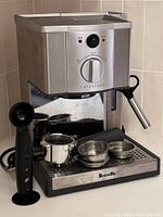 Front view of Breville Cafe Aroma espresso machine with accessories on drip tray and black measuring scoop standing next to it.