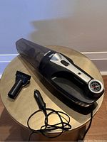 Handheld vacuum cleaner with brush attachment and power cord with car lighter plug displayed on a gold metal surface.