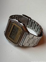 Photo of vintage Casio digital wristwatch showing gold-tone bezel with silver rubbed off and stainless steel band on a flat surface.