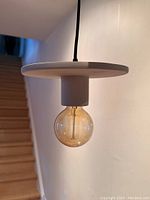 Cream coloured ceramic disk pendant light hanging from ceiling, showing the bulb and fixture profile.