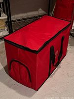 Red collapsible storage box fully assembled on floor, showing side zipper pocket and black carrying handles.