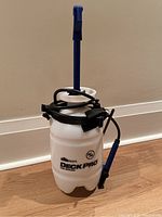 Front view of the white plastic Deck Pro pump sprayer with blue pump handle and black hose coiled around it.