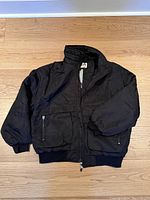 Front view of black nylon jacket laid flat, zipped closed, showing ribbed hem and cuffs