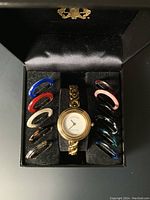 Original presentation box open showing gold plated watch at center and colored bezels arranged on either side