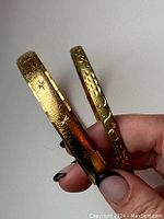 Two vintage gold plated bangle bracelets showing textured star and floral designs.