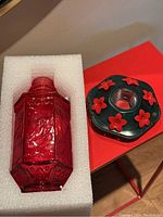 Red glass hummingbird feeder bottle and black base with red flower feeders set on a red table, cushioned in white foam packaging.