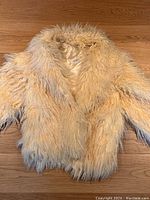 Full view of cream long-haired sheepskin coat laid flat on wooden floor