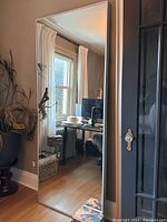 Full view of the tall standing mirror leaning against a wall showing the reflective surface and frame.