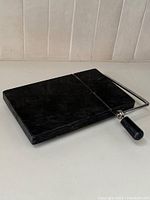 Full view of black marble cheese slicer with metal wire and handle resting on the slab surface.