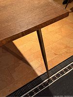 Corner detail showing veneer wood tabletop with a brass tapered leg attached, wood grain visible, some wear on edge.