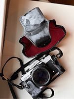 Minolta XG-9 camera with original lens and textured black grip, partially inside leather case with red fabric lining.