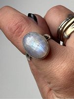 Ring worn on finger showing the oval moonstone with blue iridescence and silver band.