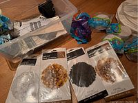 Plastic container showing packaged puff balls in white, black, gold, and mustard colors arranged alongside other decorations.