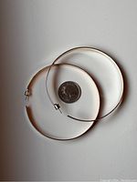 Pair of large silver hoop earrings laid flat alongside a Canadian quarter for size reference.