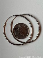 Pair of medium-sized sterling silver hoop earrings shown next to a quarter for size reference, one earring repaired at the hinge.