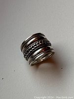 Front angle view of a wide sterling silver ring showing woven design and rope-textured edges.