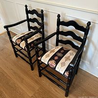 Two black finished solid wood dining chairs with geometric patterned upholstered seats in Turkish fabric, shown from a high angle on wood flooring.