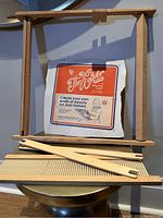 Wooden weaving loom frame with comb teeth and stick parts, original emblem sheet of 'The Weaver' weaving loom from the box.