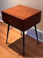 Side view showing wood top, drawer with brass pull, and black iron legs of the bedside table.