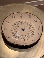 Full view of the speckled ceramic plate with zodiac symbols around the rim and starburst design with eye symbol in the center.