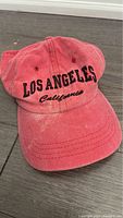 Red baseball cap with 'Los Angeles California' embroidered on front, showing signs of wear.