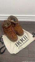 Front angle of the brown Ikki moon boots placed on the original branded drawstring bag.